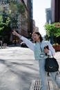 Businesswoman with a bag hailing a taxi in a vibrant city street on a sunny day.